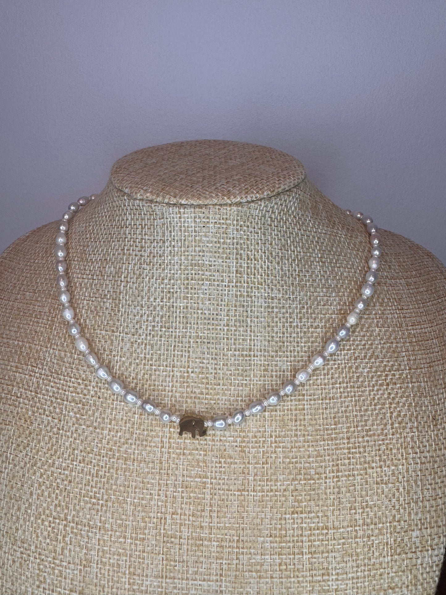 A freshwater pearl necklace with a silver pendant in the shape of an elephant, displayed on a mannequin.