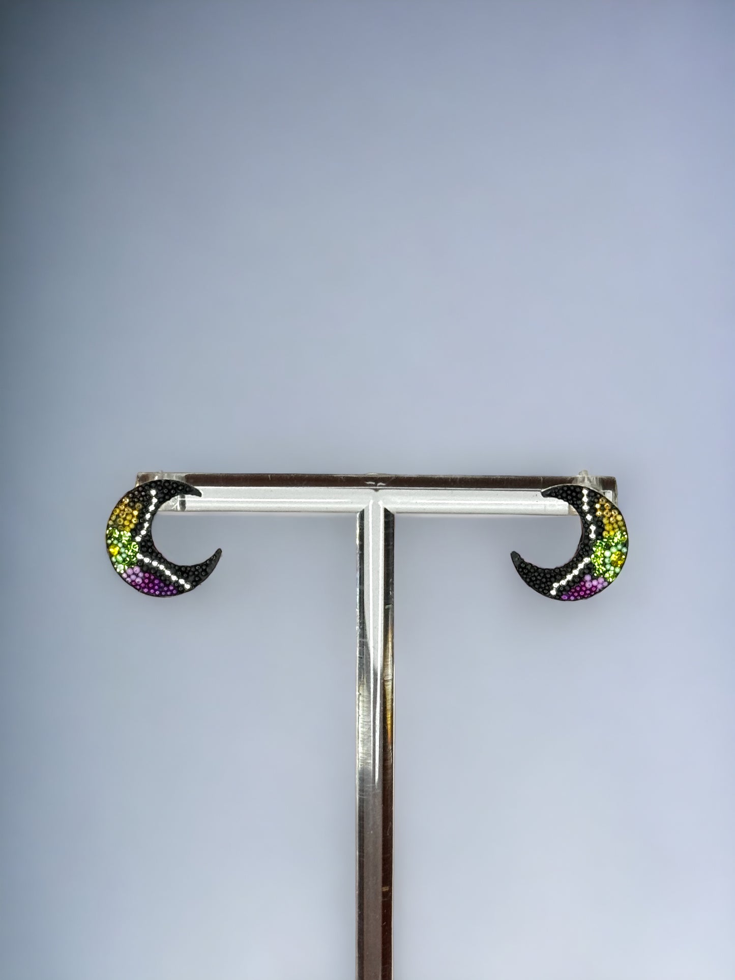 A pair of black half moon shaped earrings embellished with green, yellow, and purple crystals, mounted on a silver 925 studs style earring post.