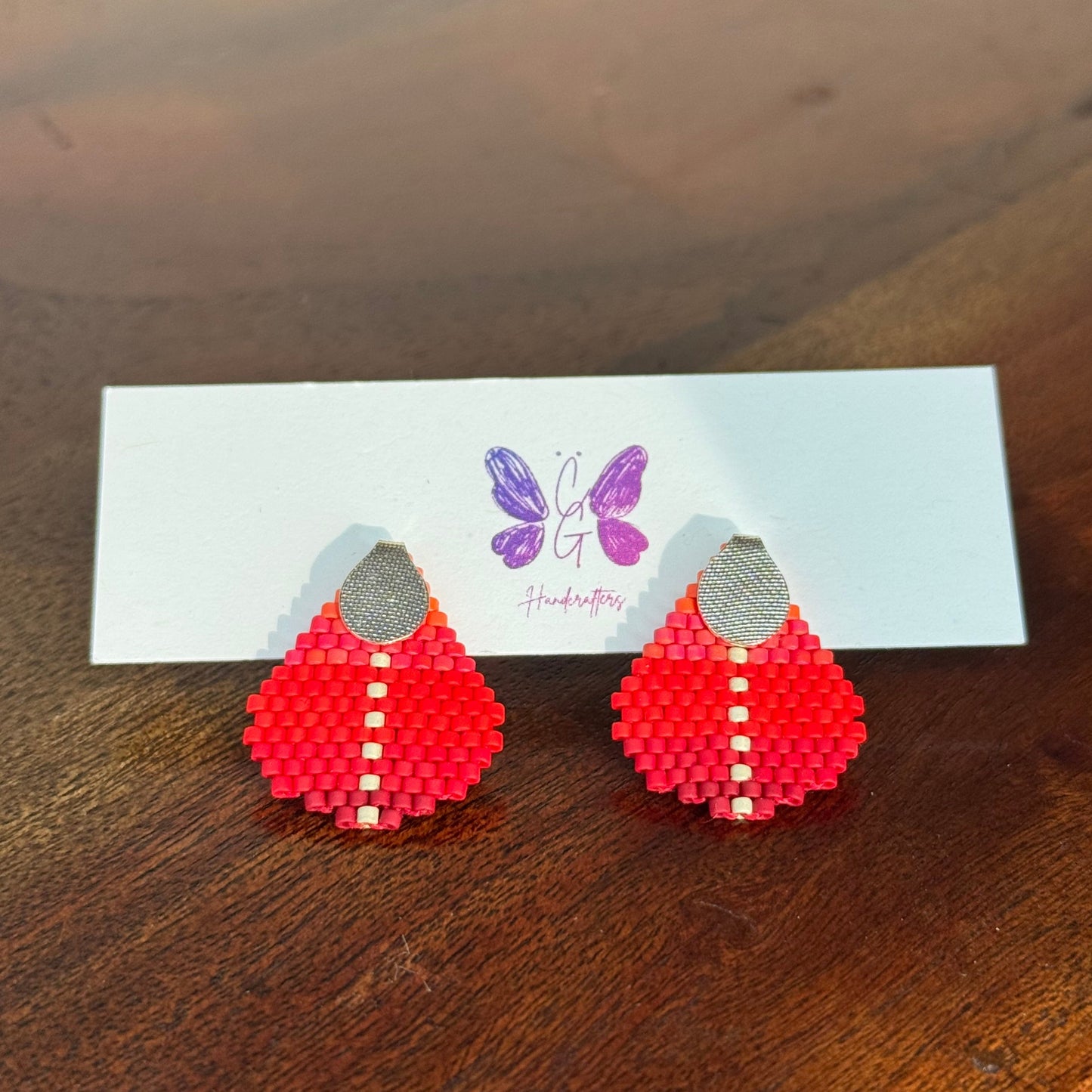 Red beaded earrings on a white card with a purple logo on a wooden surface