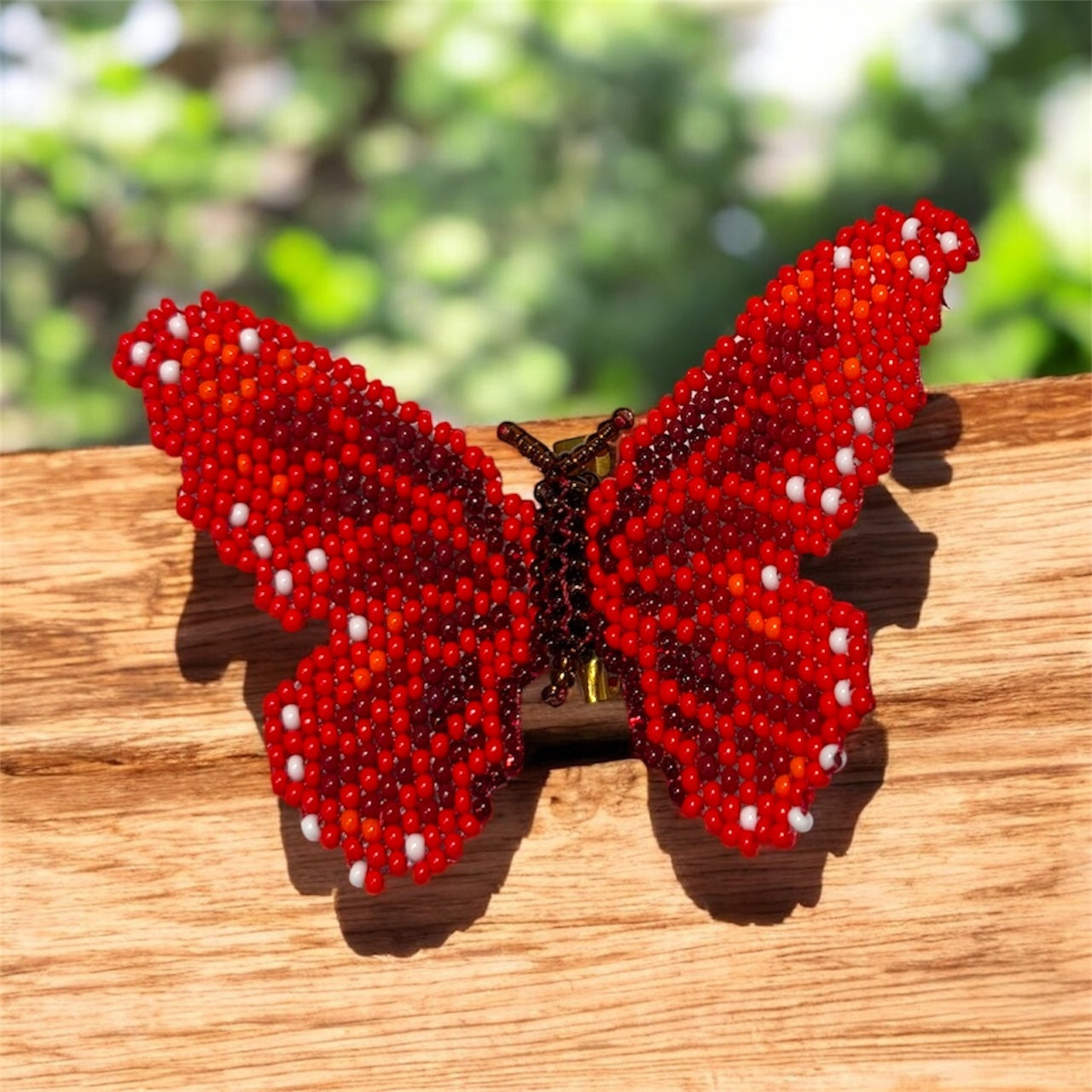 Red beaded butterfly on a wooden surface with a blurred natural background