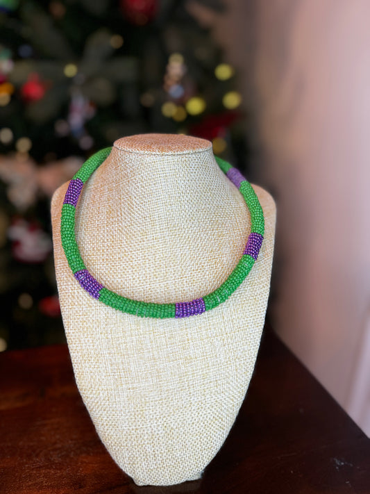 A green and purple crochet necklace with a lobster claw clasp displayed on a mannequin.