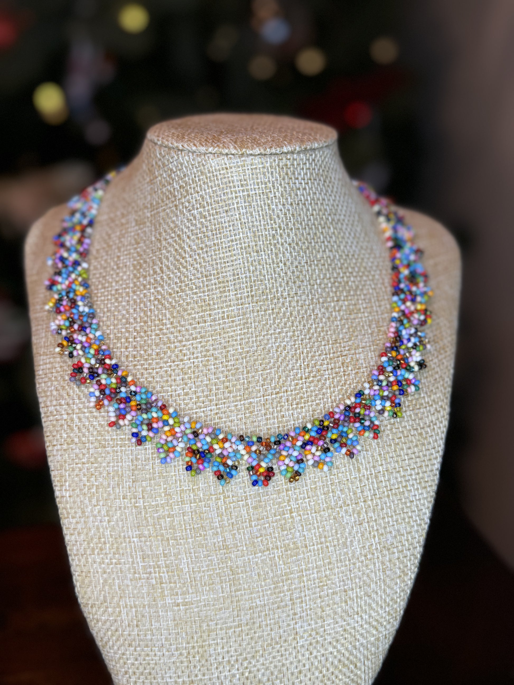 A multicolored beaded necklace displayed on a mannequin bust, featuring a variety of colorful beads and leaf-shaped ends.