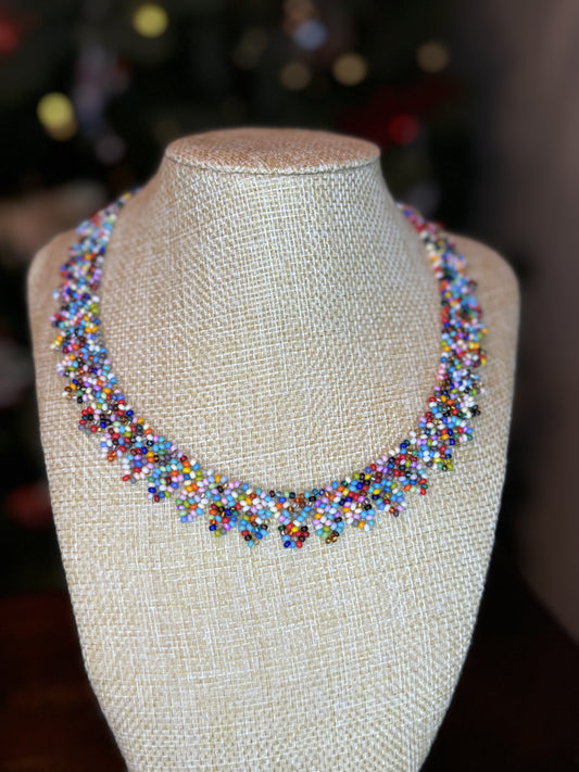 A multicolored beaded necklace displayed on a mannequin bust, featuring a variety of colorful beads and leaf-shaped ends.