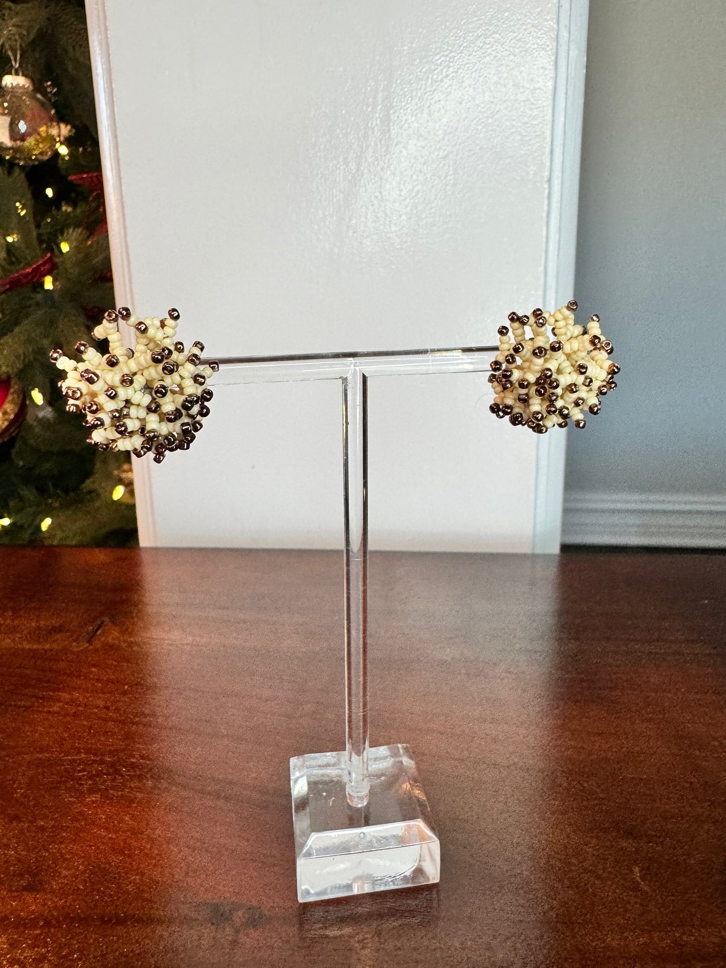 A pair of beige and pecan colored earrings with a stud-style design, displayed on a clear stand.