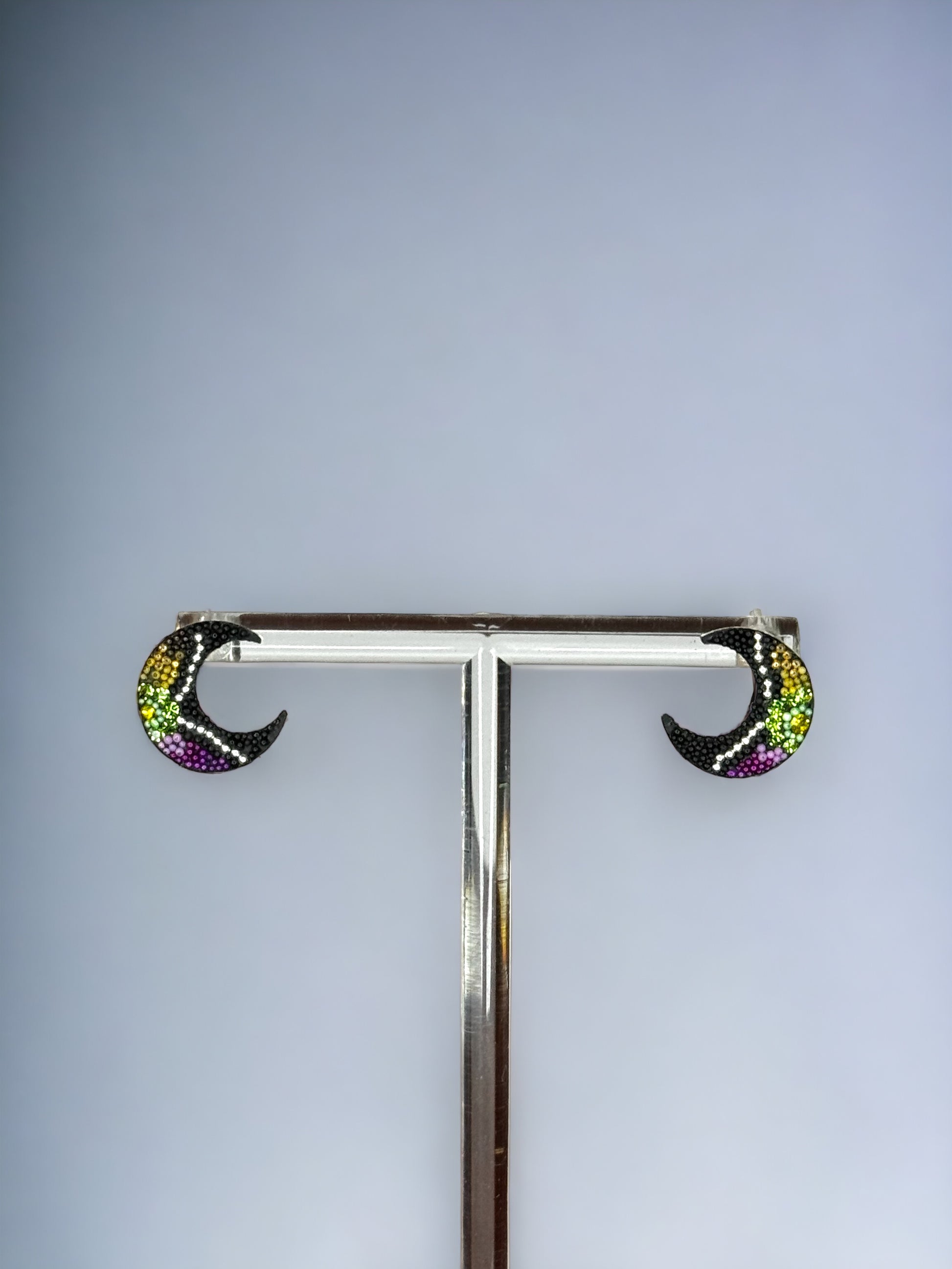 A pair of black half moon shaped earrings embellished with green, yellow, and purple crystals, mounted on a silver 925 studs style earring post.