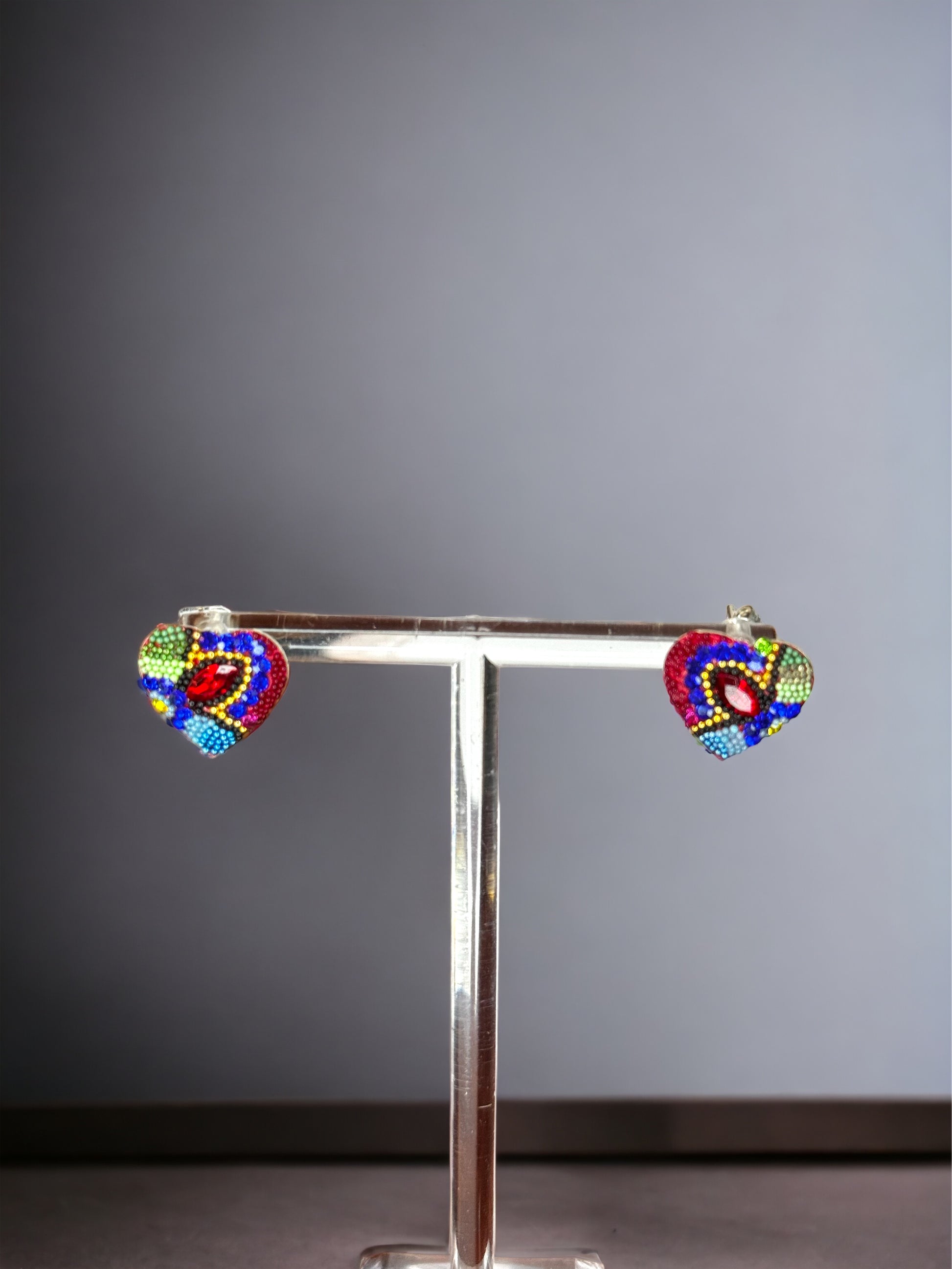 A pair of heart-shaped stud earrings, with red, blue, and green Swarovski crystals, mounted on a silver 925 
