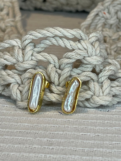 A pair of pearl stick studs with gold plating and rope-like texture on the back, displayed on a textured surface.