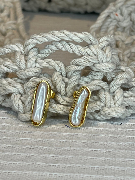 A pair of pearl stick studs with gold plating and rope-like texture on the back, displayed on a textured surface.