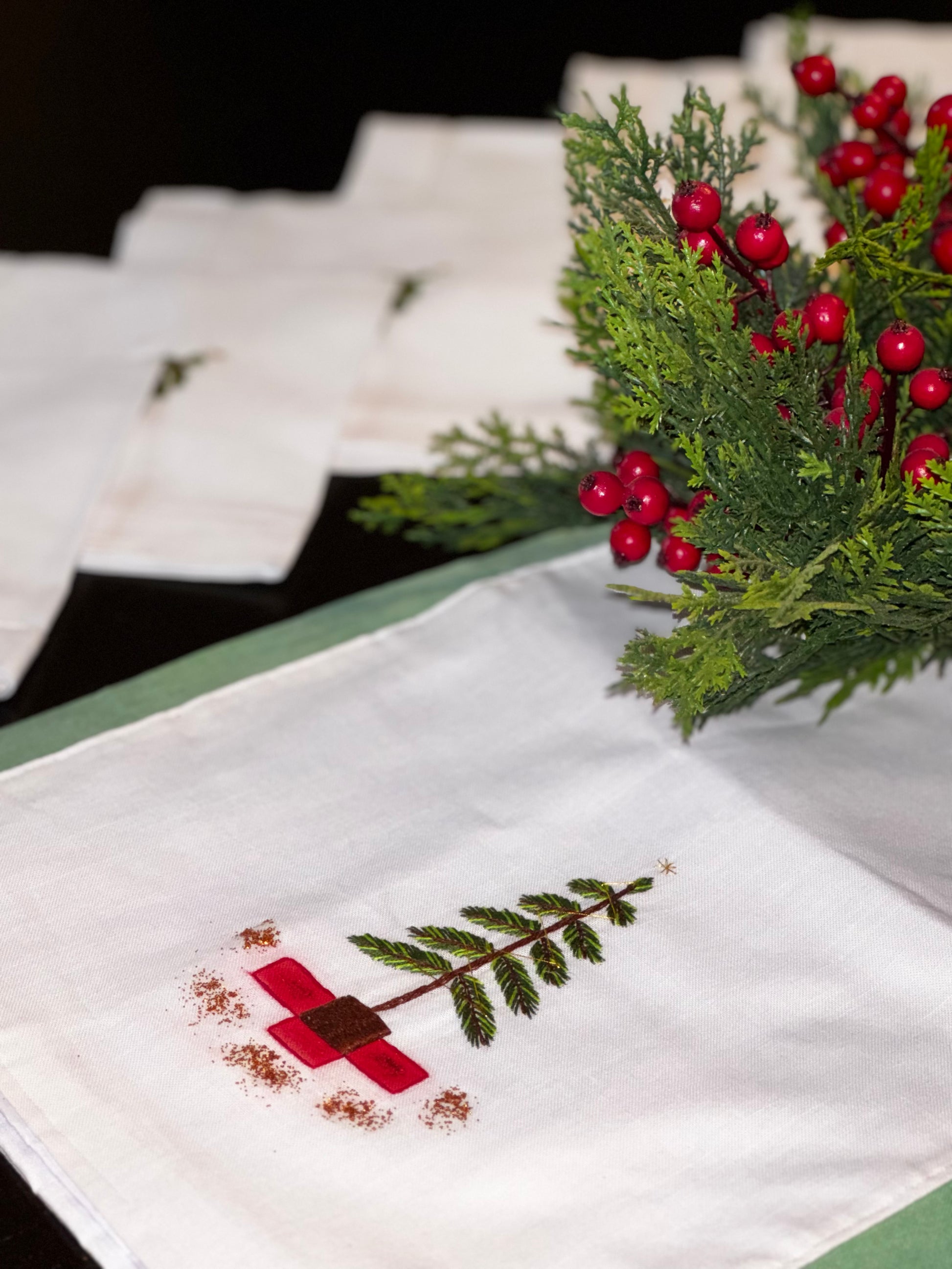 A set of white linen napkins with a Christmas tree embroidered in the center, displayed on a table