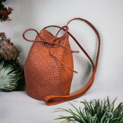 A terracota wicker bucket bag with a drawstring closure,