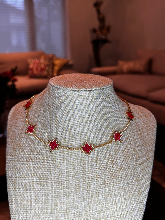 A red and gold choker necklace with a delicate brick stick technique, displayed on a mannequin.