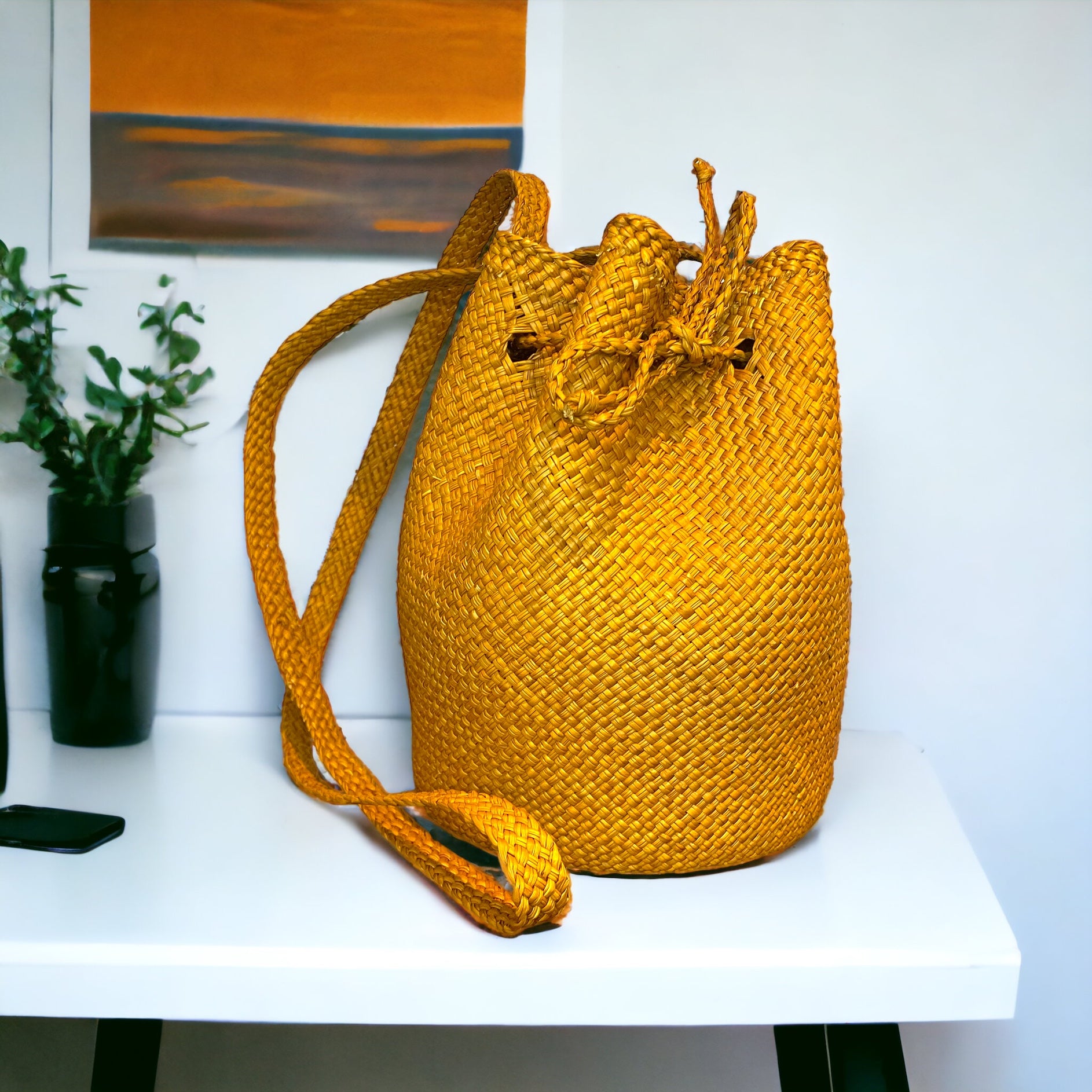 A yellow wicker bucket bag with a drawstring closure, placed on a white surface with a blurred background.