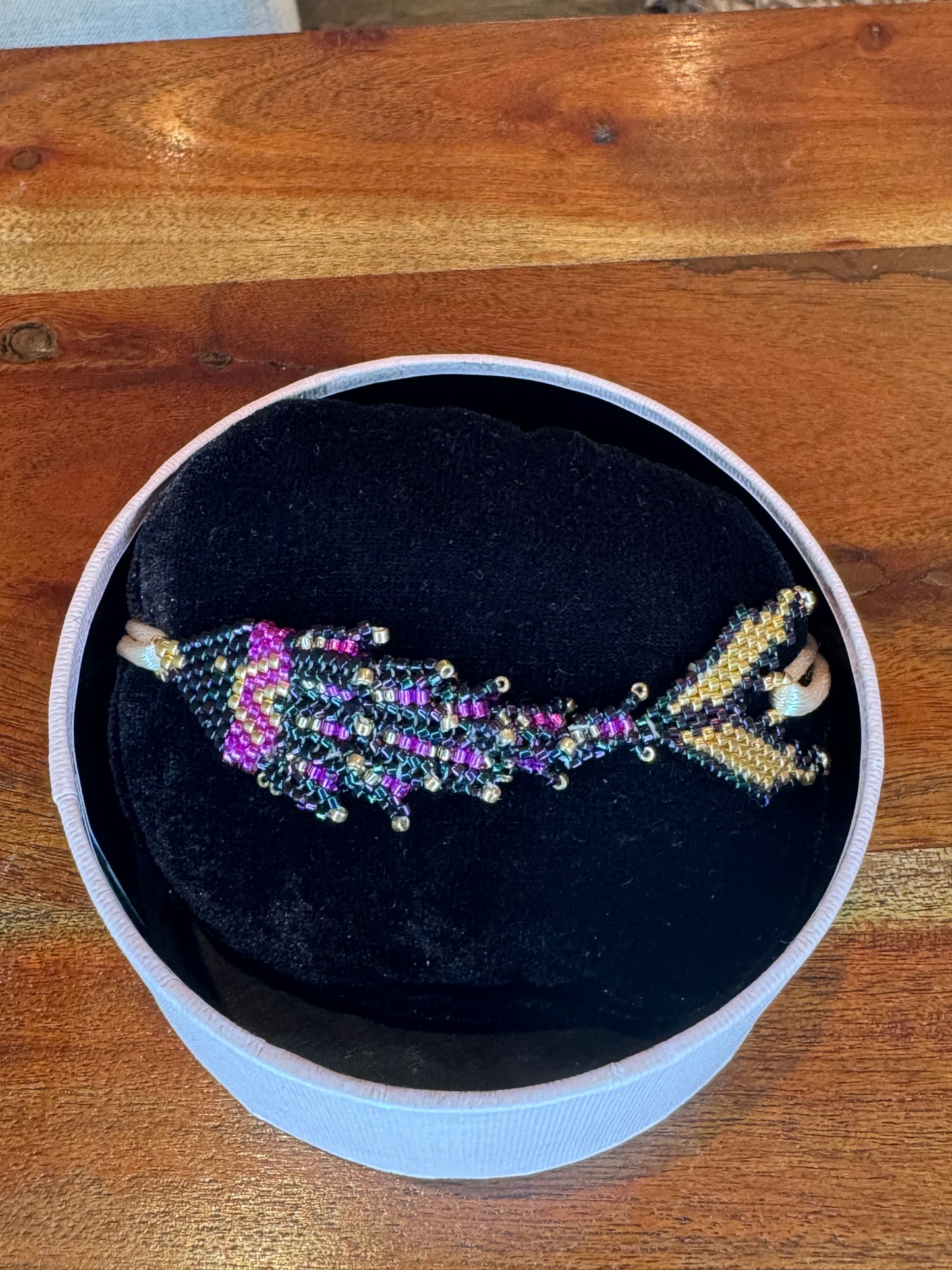 A Pez-shaped bracelet made of multicolored beads, displayed on a round box.