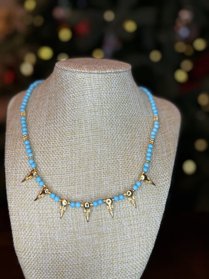 A turquoise beaded necklace with gold-plated accents displayed on a mannequin. The necklace features a unique design with geometric shaped pendants.