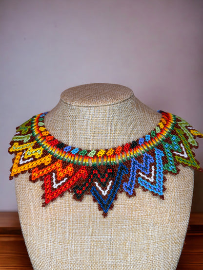A colorful beaded necklace displayed on a mannequin bust, featuring a variety of geometric patterns.