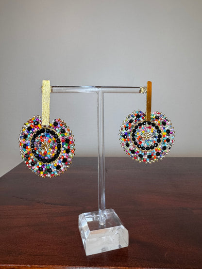 A pair of Spark Earrings displayed on a stand, featuring a hypoallergenic German silver stud and blue acrylic crystals in a circular beaded design.