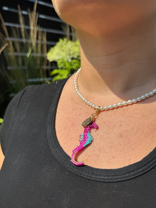 Person wearing a black top with a colorful seahorse charm on a pearl necklace.