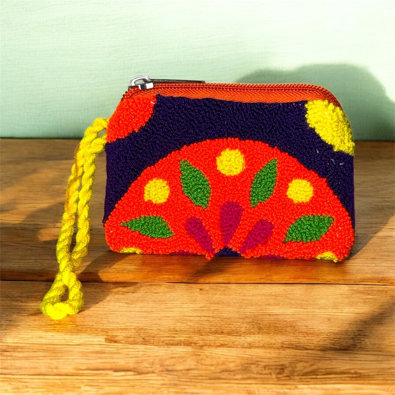 Colorful handcrafted pouch with a yellow strap on a wooden surface