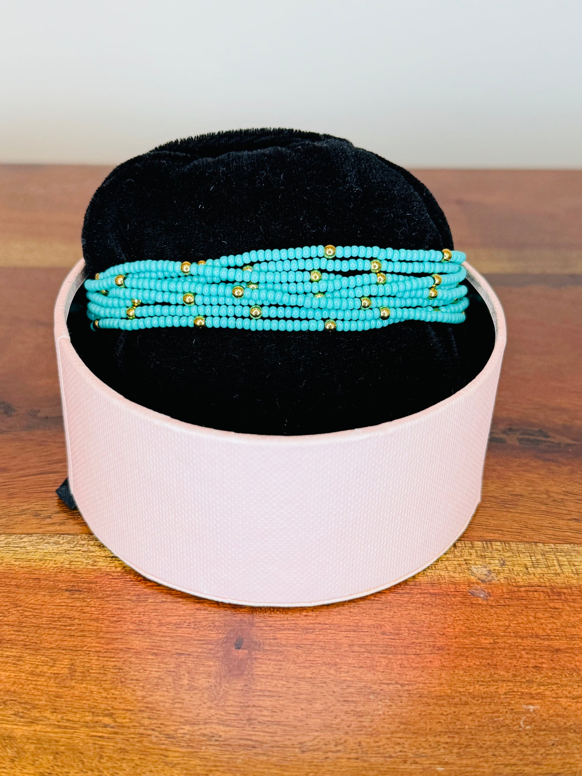 A multi-colored beaded bracelet displayed on a white stand with a black base, set on a wooden surface.