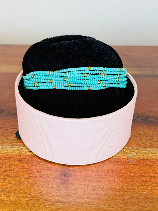 A multi-colored beaded bracelet displayed on a white stand with a black base, set on a wooden surface.