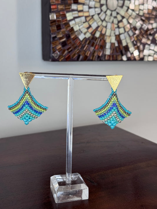 A pair of triangular-shaped aquamarine, gold, and green beaded earrings on display against a tiled background.