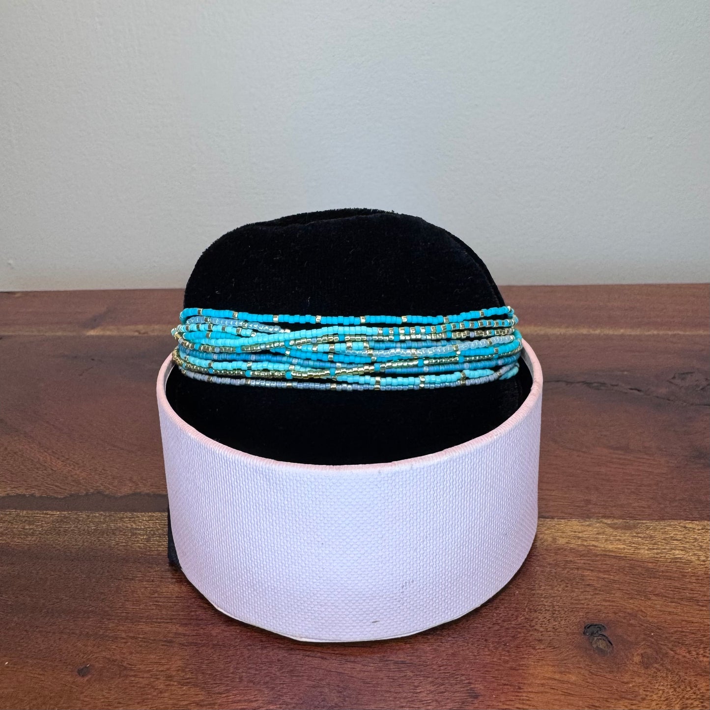 Black headband with blue beaded bands on a white cylindrical container against a plain background