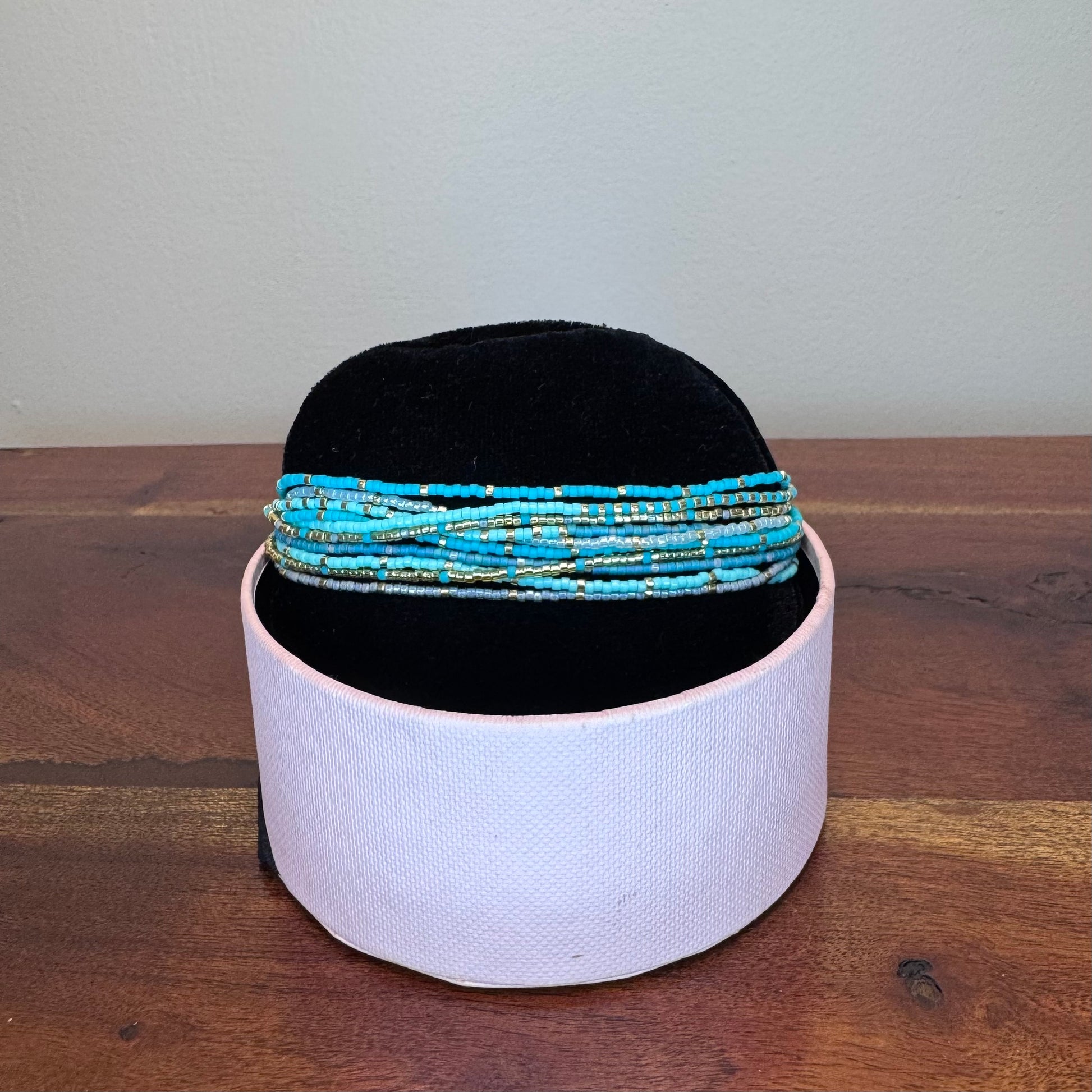 Black headband with blue beaded bands on a white cylindrical container against a plain background