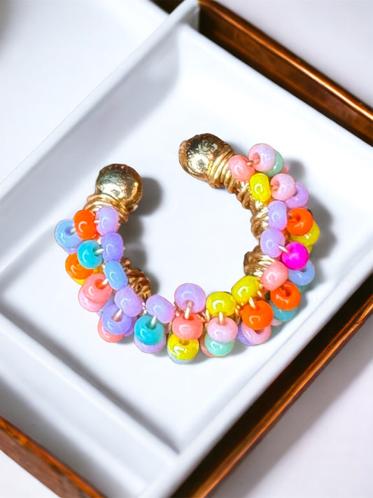 A multicolored beaded ear cuff displayed on a white surface, with the colors of the beads resembling a rainbow arch.