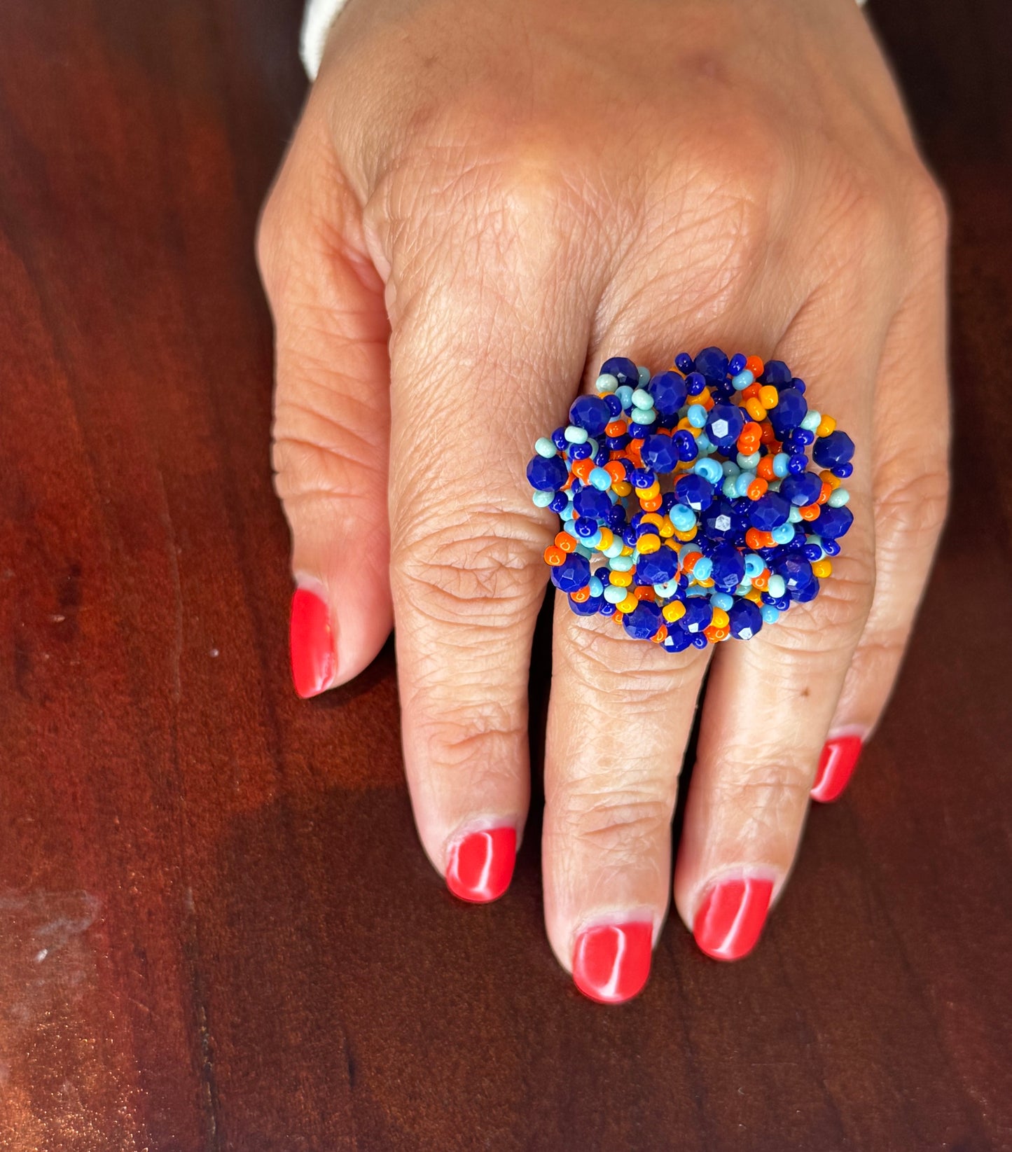 A colorful woven beaded ring displayed on a person's finger with red nail polish.
