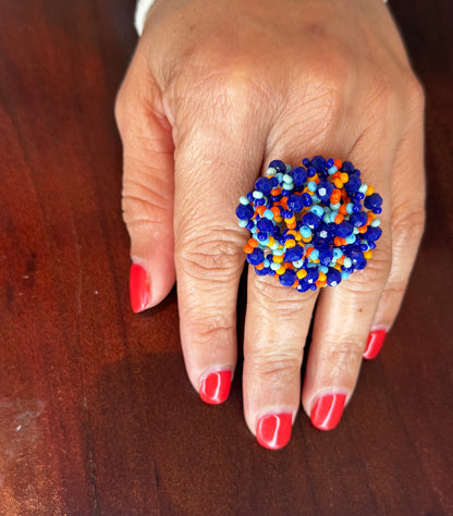 A colorful woven beaded ring displayed on a person's finger with red nail polish.