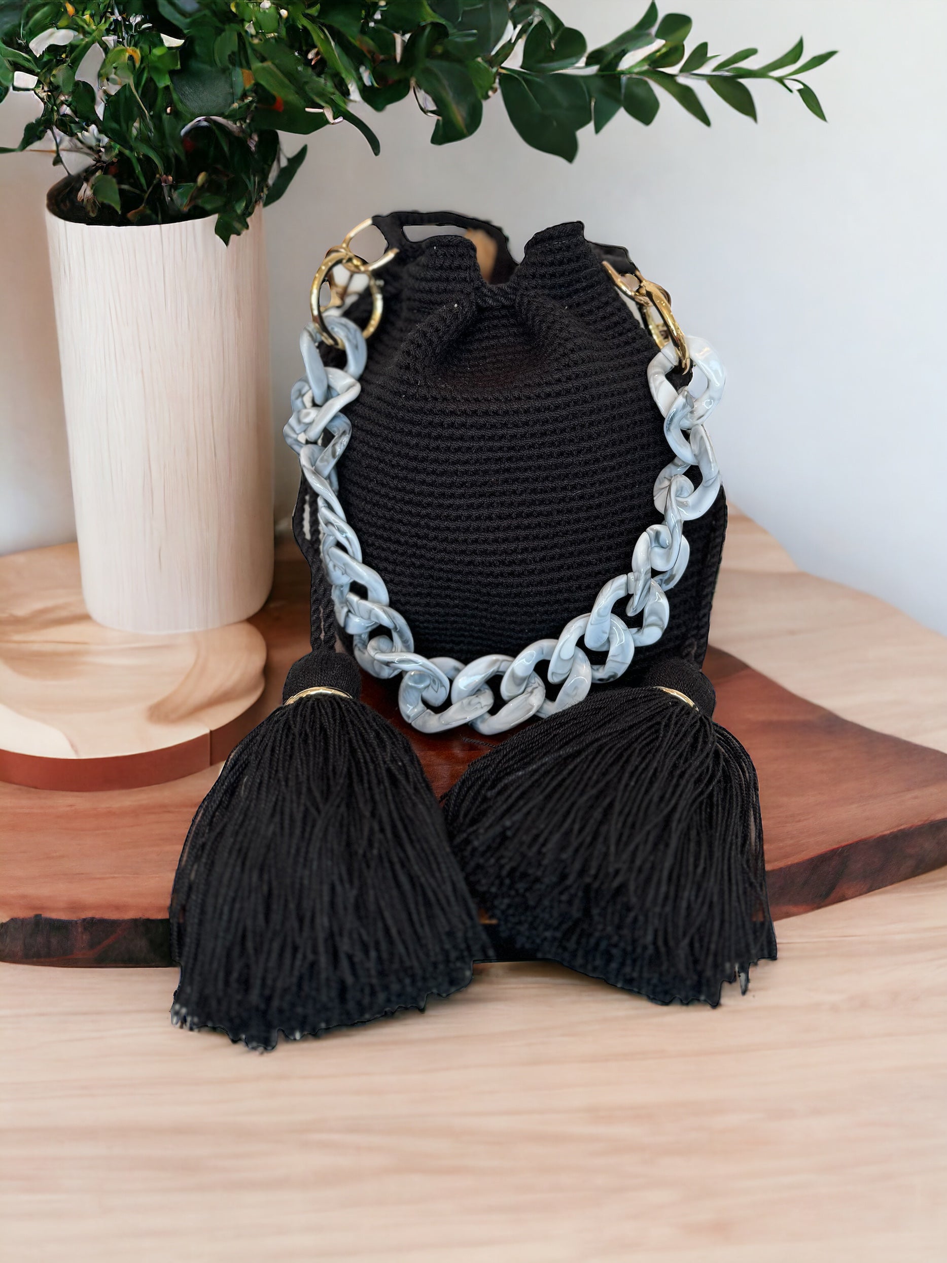 A black Lux Mochila handbag with a chain strap and tassel detail displayed on a wooden surface.