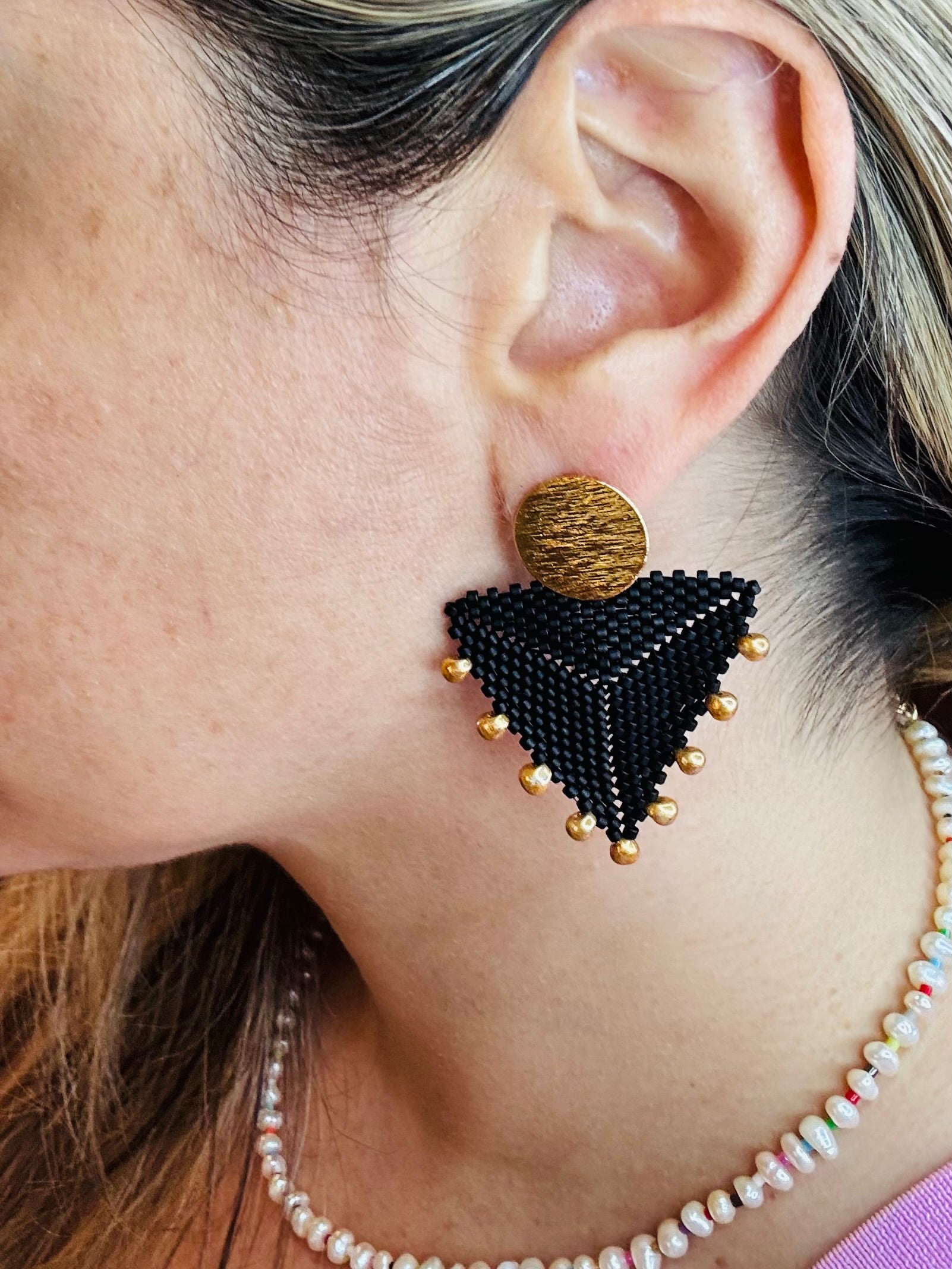 Close-up of an ear wearing a black beaded triangle earring with a gold accent.
