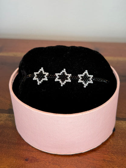 A bracelet with purple and gold colors displayed on a black cushion inside a pink box.
