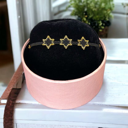 A bracelet with purple and gold colors displayed on a black cushion inside a pink box.