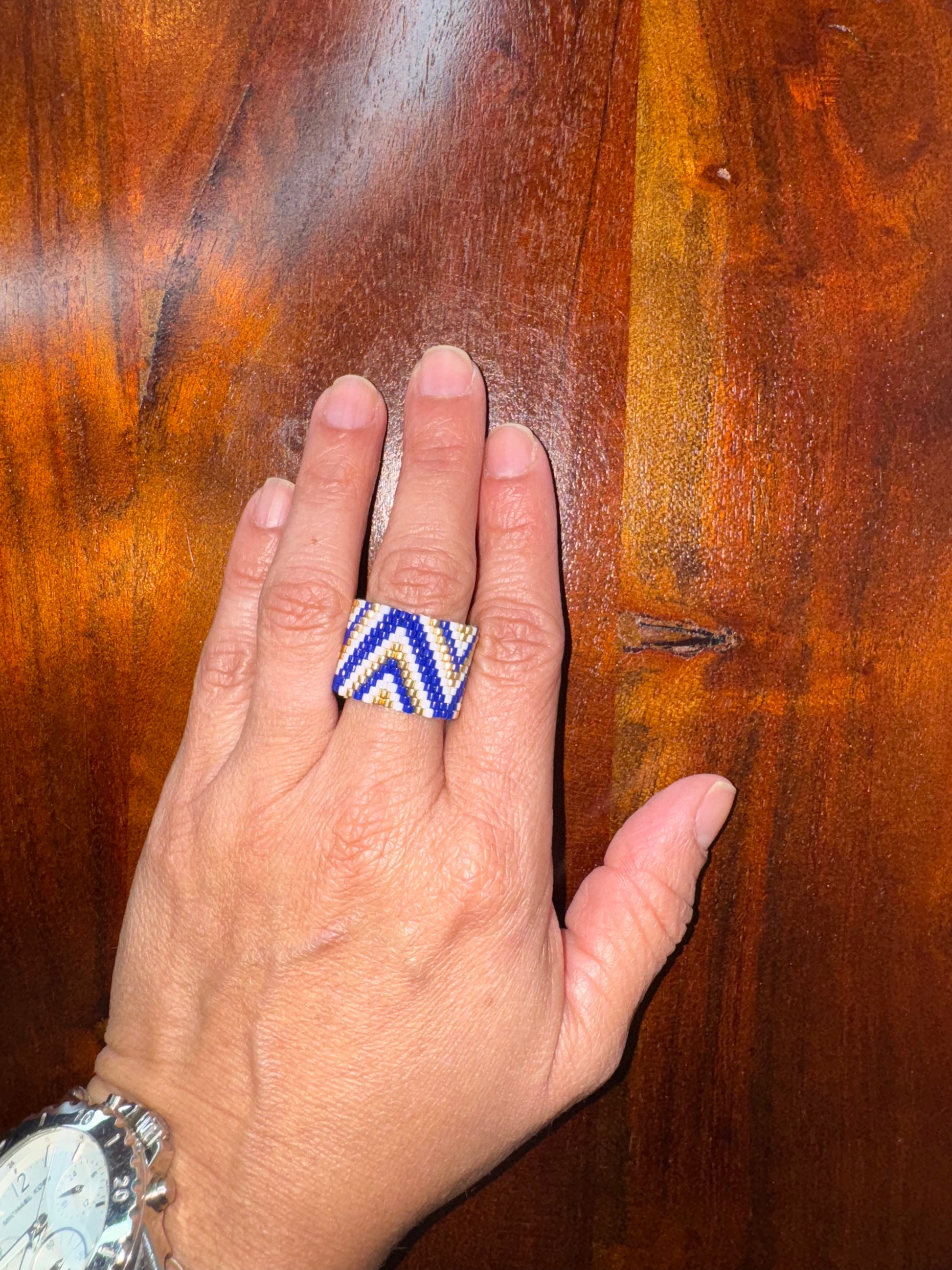 Hand wearing a blue and white zigzag ring on a wooden surface