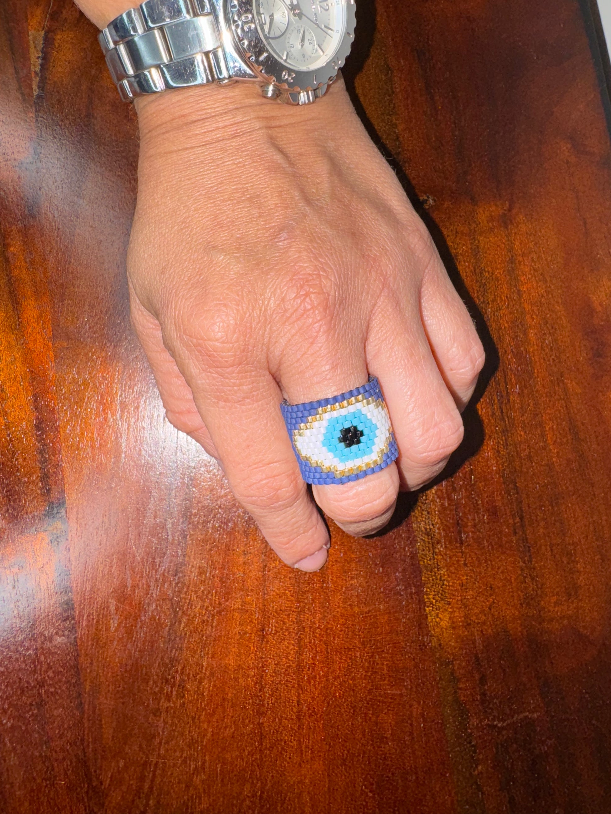 Hand wearing a blue beaded ring on a wooden surface