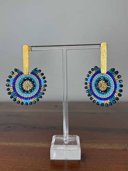A pair of Spark Earrings displayed on a stand, featuring a hypoallergenic German silver stud and blue acrylic crystals in a circular beaded design.