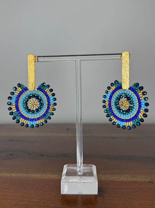 A pair of Spark Earrings displayed on a stand, featuring a hypoallergenic German silver stud and blue acrylic crystals in a circular beaded design.