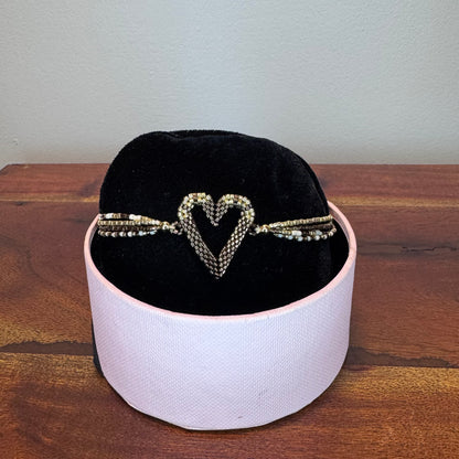 Bracelet with a heart design on a black cushion inside a white box on a wooden surface.