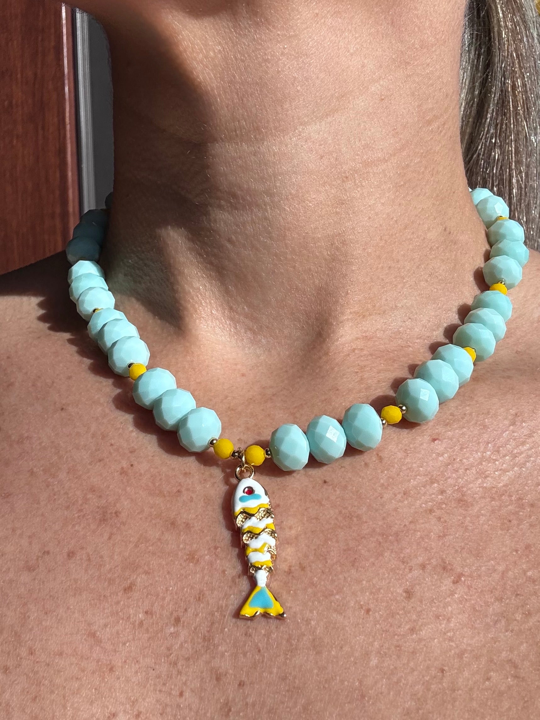 Necklace with light blue beads and a fish charm on a person's neck.