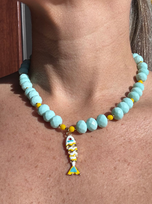 Necklace with light blue beads and a fish charm on a person's neck.