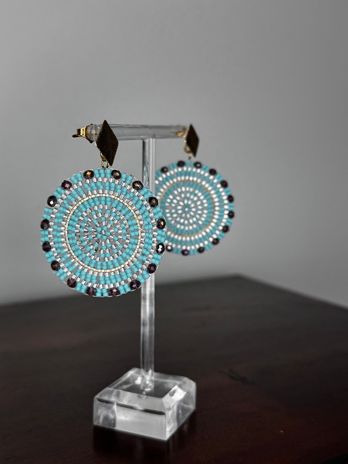 A pair of Spark Earrings displayed on a stand, featuring a hypoallergenic German silver stud and blue acrylic crystals in a circular beaded design.