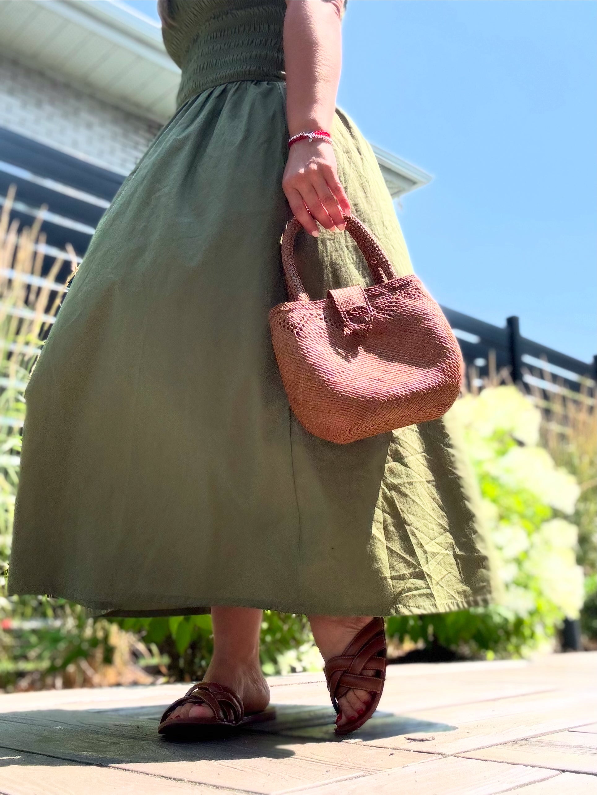 Person wearing a green dress holding a pink handbag outdoors.