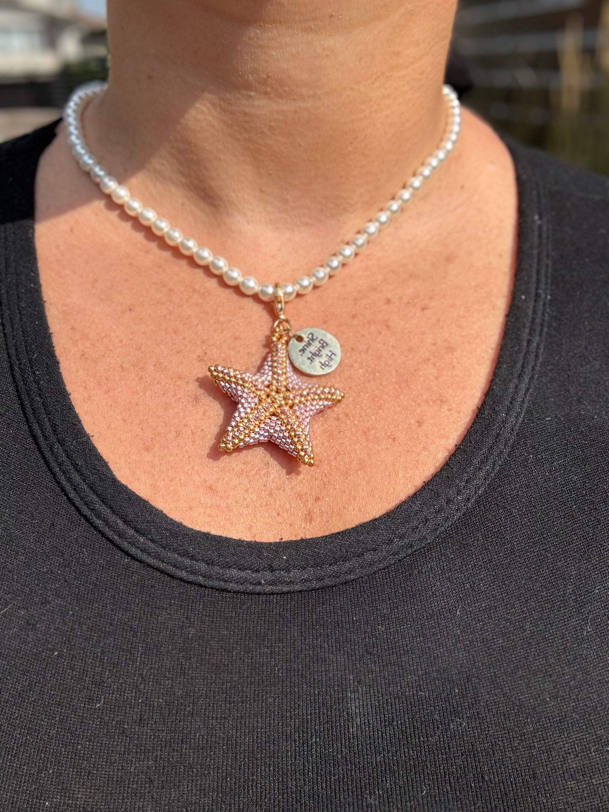 Pearl necklace with a star-shaped pendant worn by a person against a blurred background