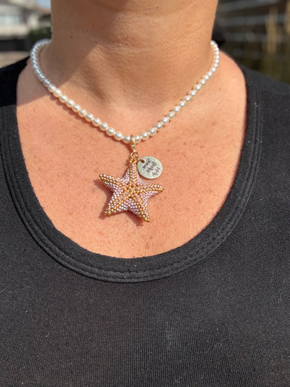 Pearl necklace with a star-shaped pendant worn by a person against a blurred background