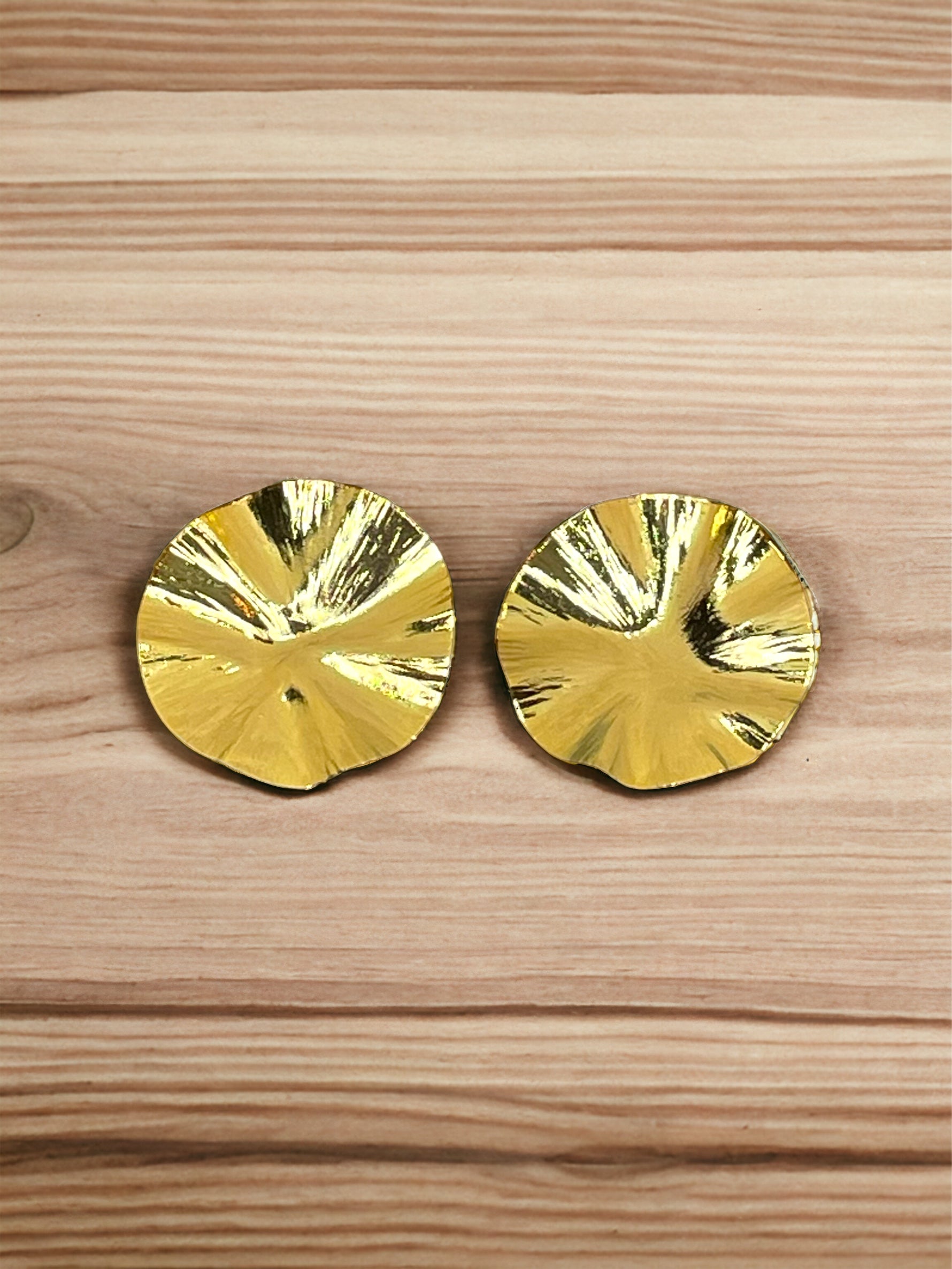 A pair of gold-plated bronze wrinkle earrings with a round shape, displayed on a wooden surface.