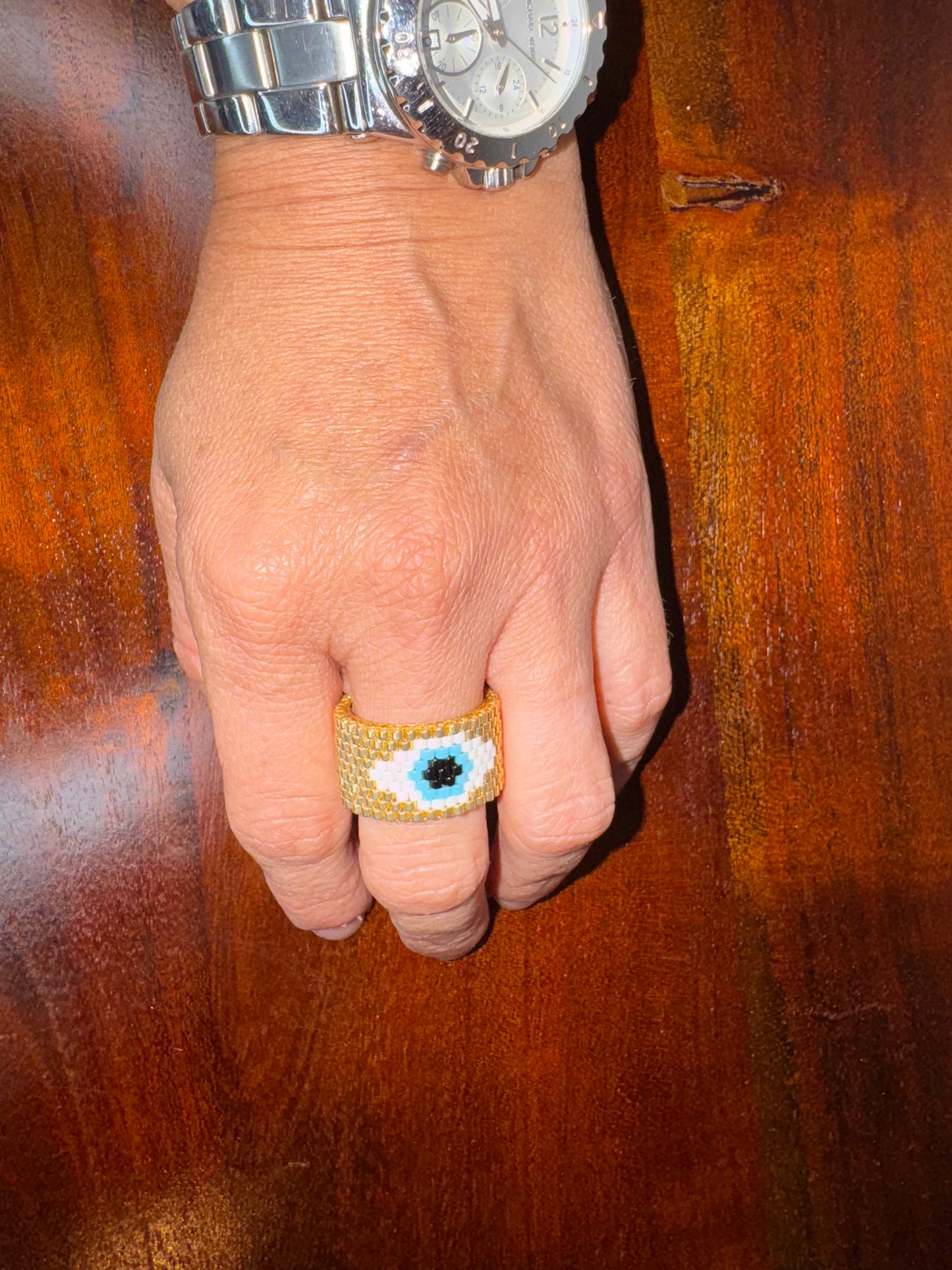 Hand wearing a silver watch and a decorative ring on a wooden surface