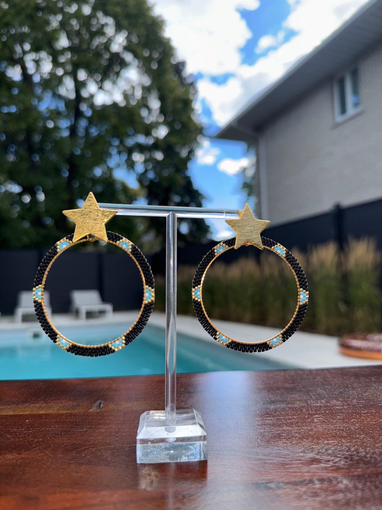 Pair of earrings with star and moon designs on a stand outdoors.