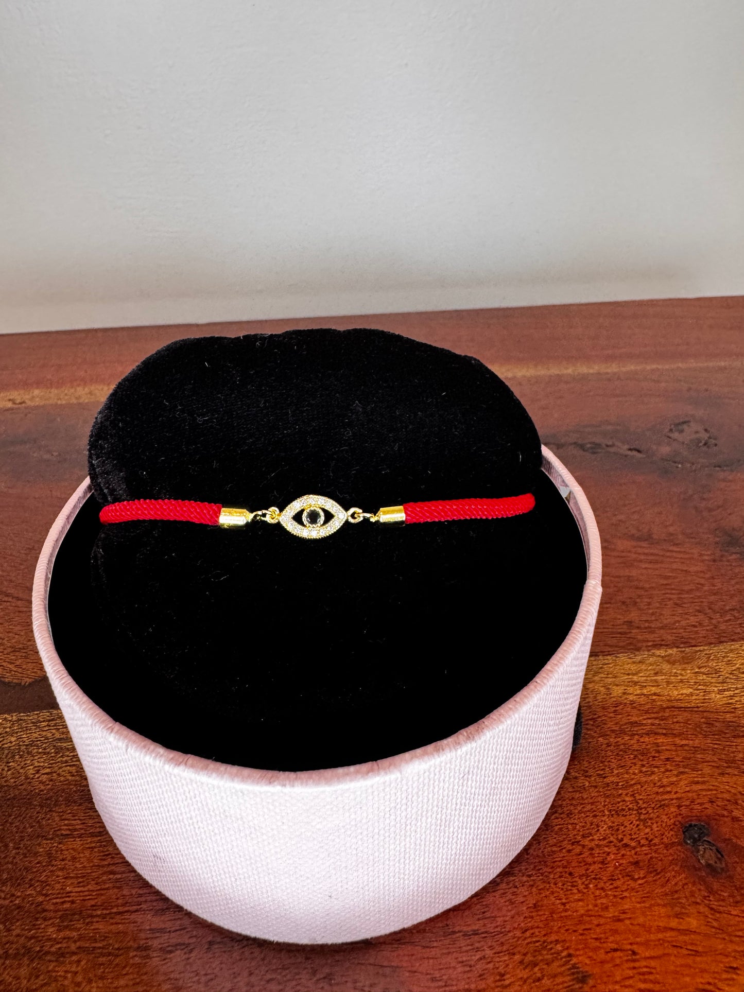 Decorative pendant with red string and gold accents on a black cushion inside a white container on a wooden surface.