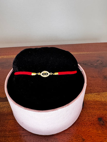 Decorative pendant with red string and gold accents on a black cushion inside a white container on a wooden surface.